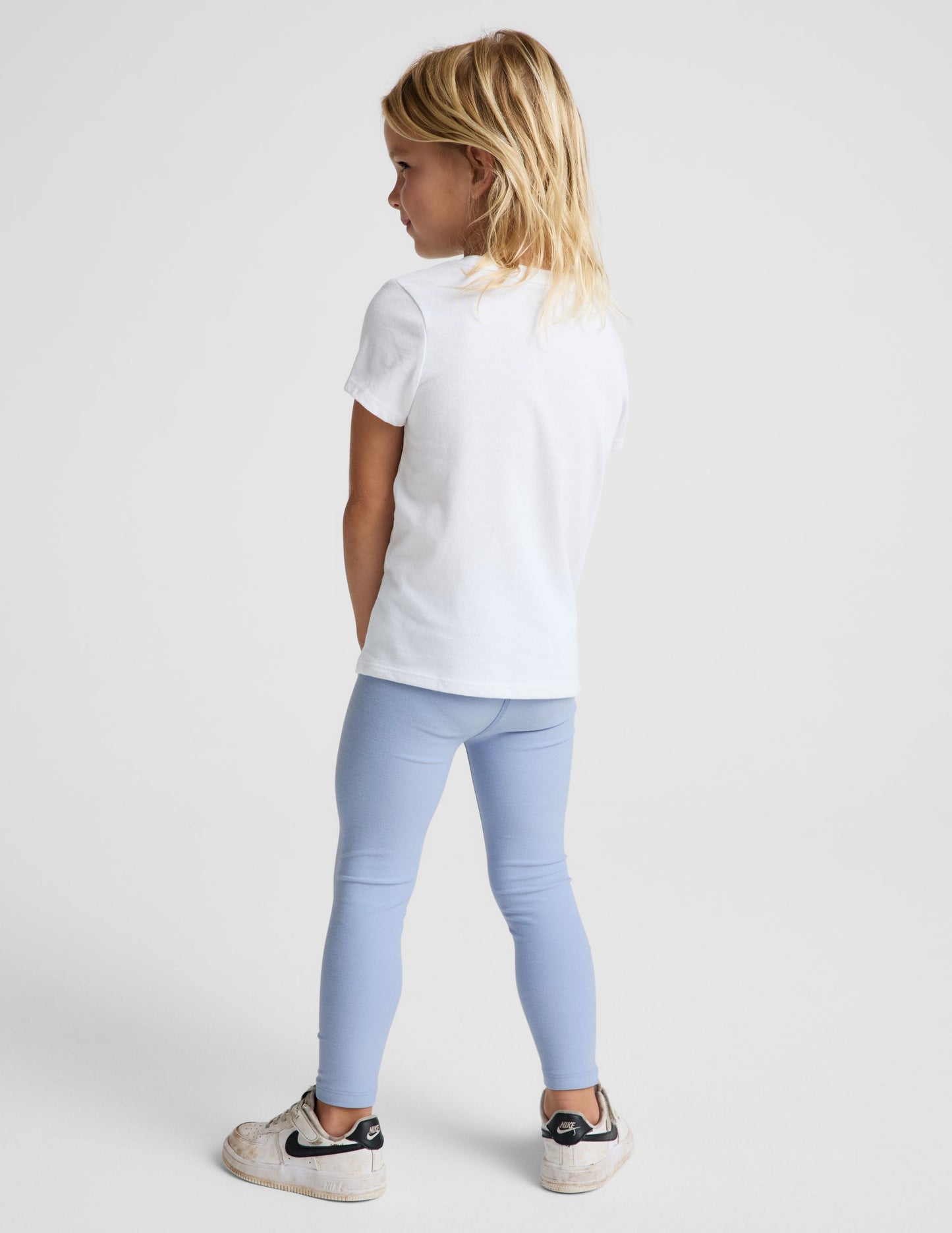Girl wearing Blue Spacedye™ Toddler Legging paired with a white t-shirt and white sneakers, rear view.