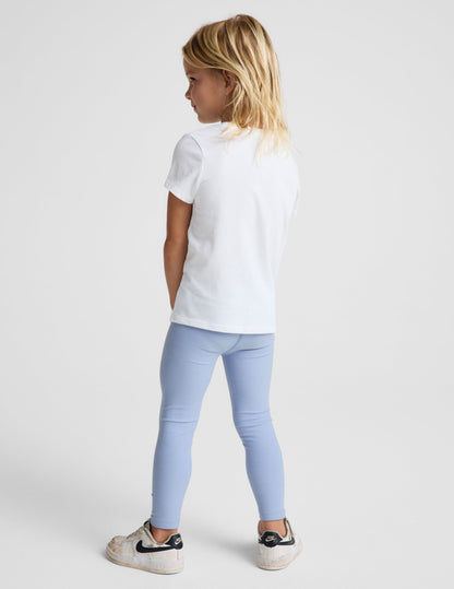 Girl wearing Blue Spacedye™ Toddler Legging paired with a white t-shirt and white sneakers, rear view.