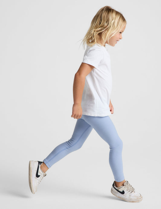 Girl wearing Blue Spacedye™ Toddler Legging paired with a white t-shirt and sneakers in a side profile view.