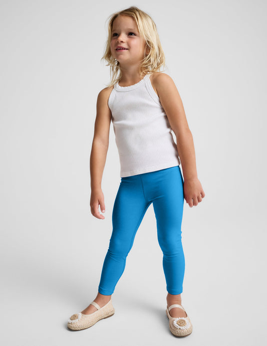 Girl wearing Blue Spacedye™ Toddler Legging paired with a white ribbed tank top and tan ballet flats.