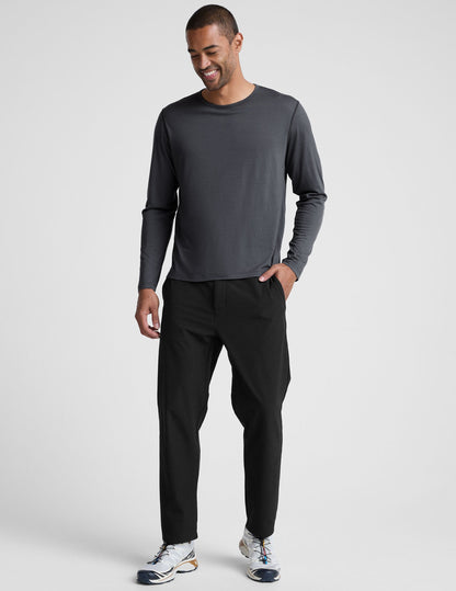 Man wearing a dark gray crew neck long sleeve and black pants against a light background.