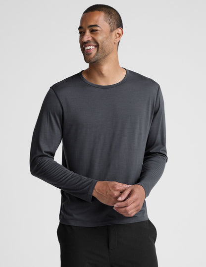 Man wearing a dark gray crew neck long sleeve and black pants against a light background.
