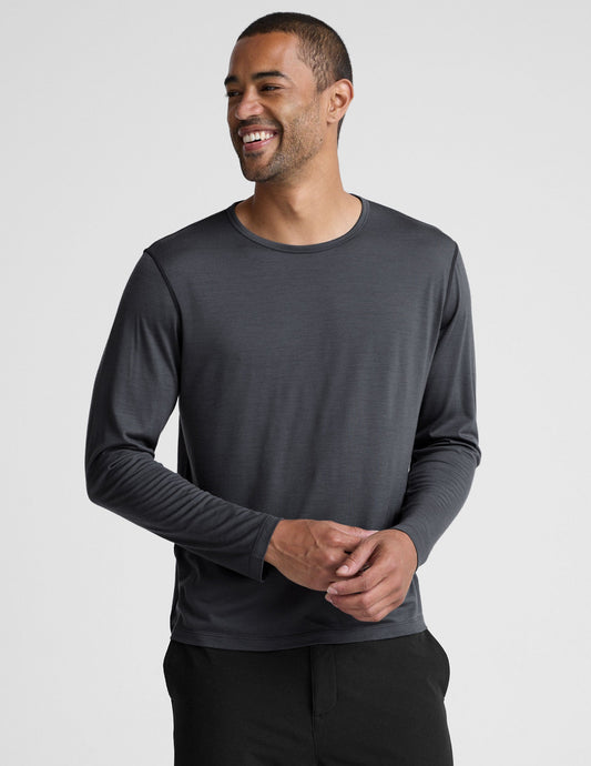 Man wearing a dark gray crew neck long sleeve and black pants against a light background.