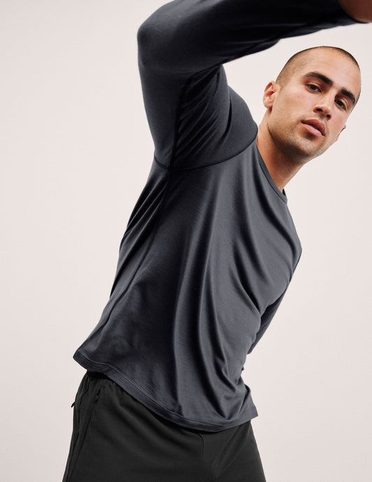 Man wearing a dark gray crew neck long sleeve and black pants stretching against a light background.