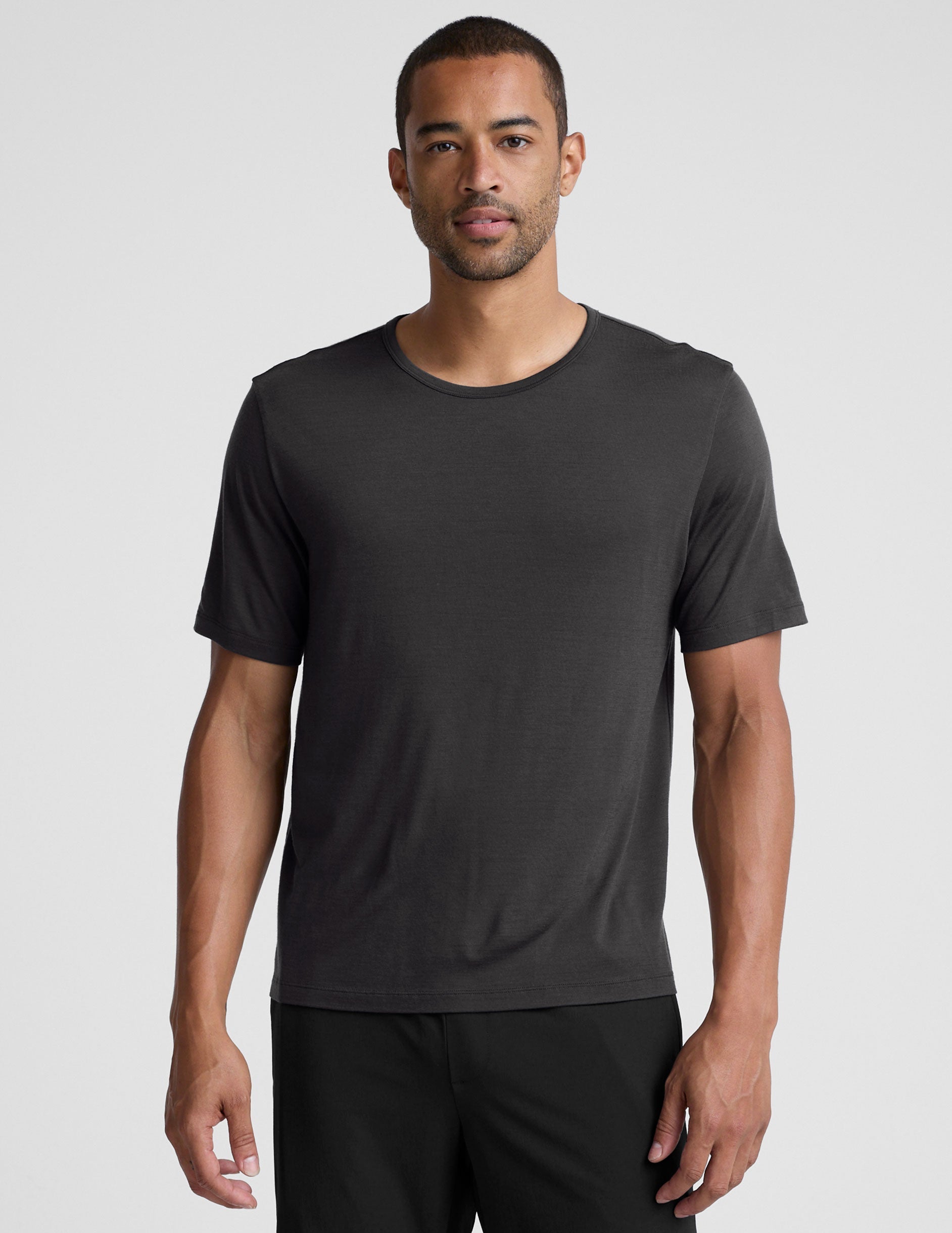 man wearing a black t-shirt and pants on a plain background.