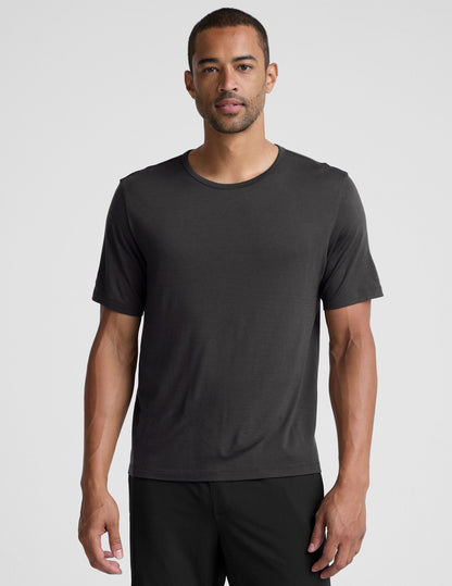 man wearing a black t-shirt and pants on a plain background.