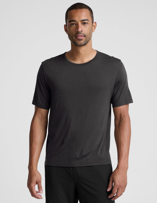 man wearing a black t-shirt and pants on a plain background.