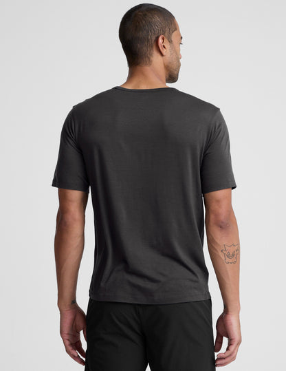 man wearing a black t-shirt and pants on a plain background.