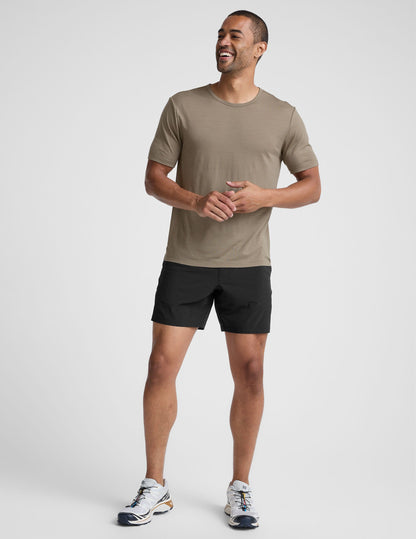 Man wearing a beige t-shirt and black shorts on a light gray background.