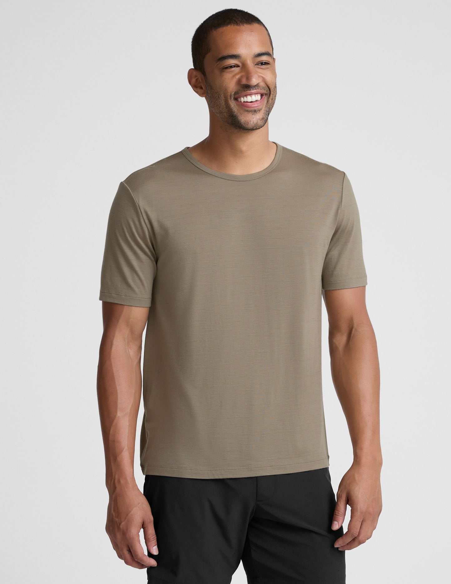Man wearing a beige t-shirt and black shorts on a light gray background.