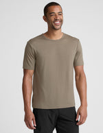 Man wearing a beige t-shirt and black shorts on a light gray background.