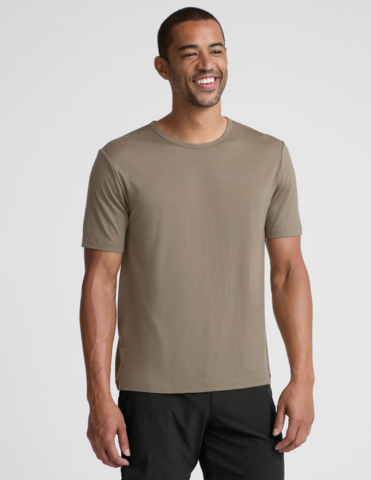 Man wearing a beige t-shirt and black shorts on a light gray background.