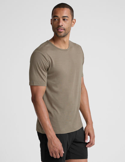 Man wearing a beige t-shirt and black shorts on a light gray background.