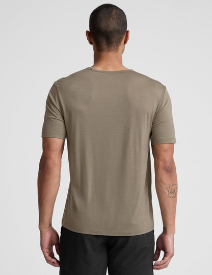 Man wearing a beige t-shirt and black shorts on a light gray background.