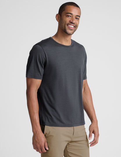 Man wearing a dark gray t-shirt and beige pants on a white background.