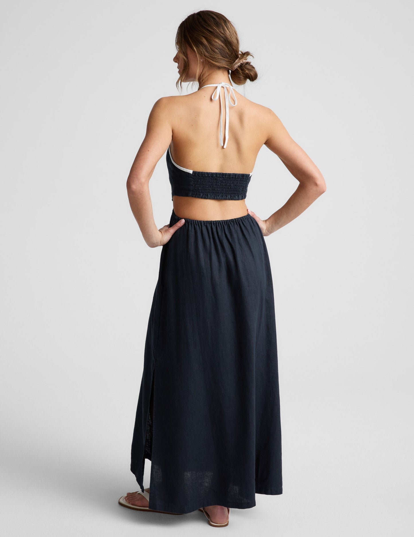 Woman wearing a navy blue halter neck midi dress on a light gray background.