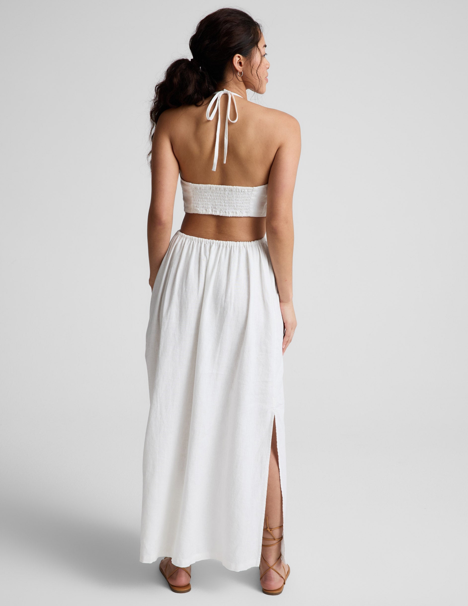 Woman wearing a white midi length halter dress against a plain background.