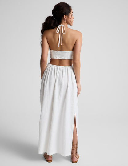 Woman wearing a white midi length halter dress against a plain background.