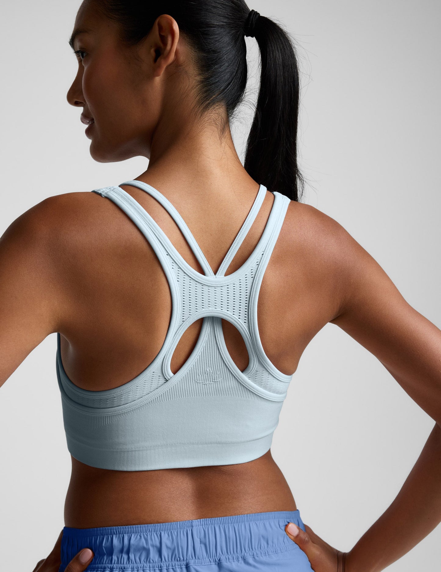 Woman wearing a light blue sports bra and shorts on a plain background.