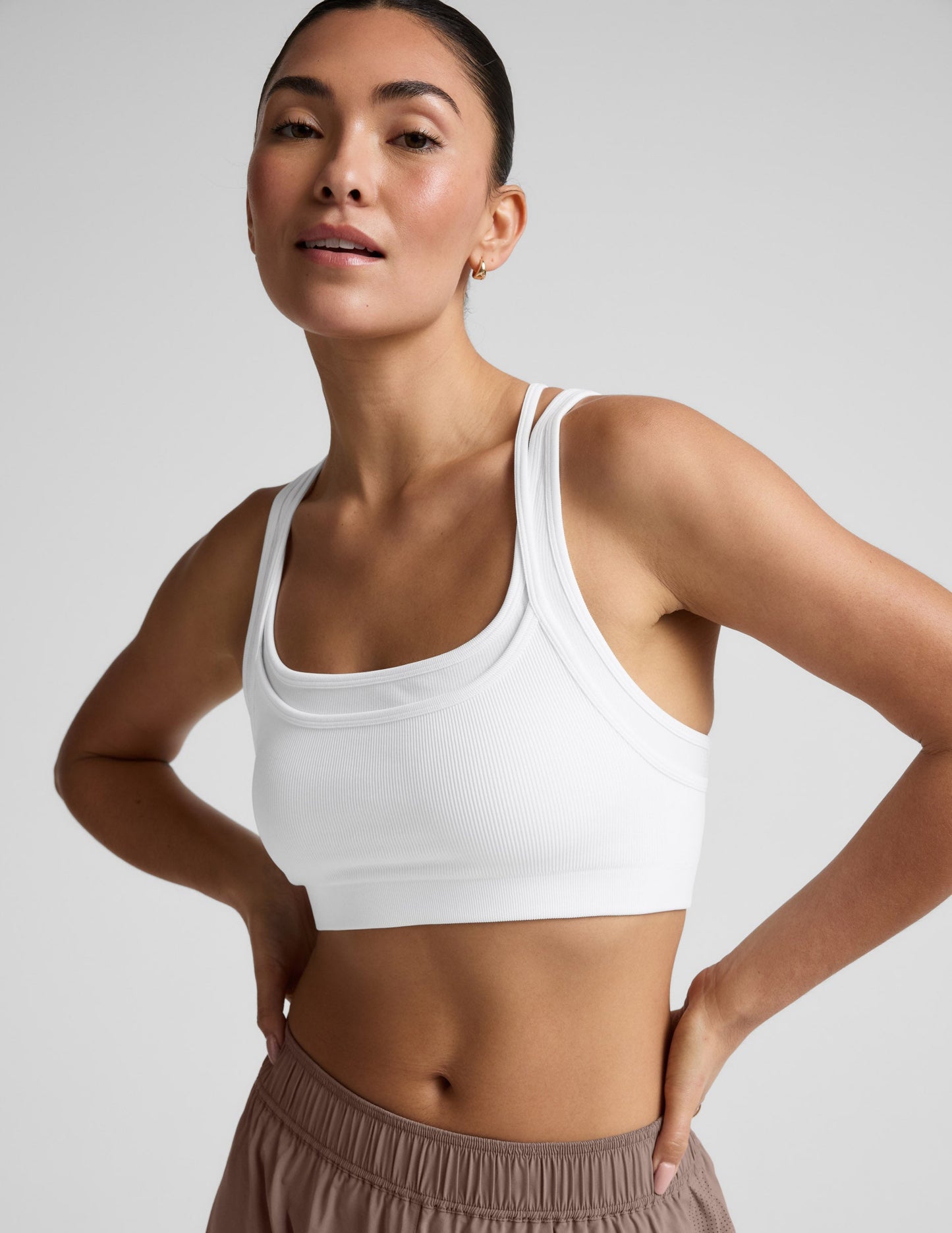 Woman wearing a white sports bra and brown shorts on a plain background.