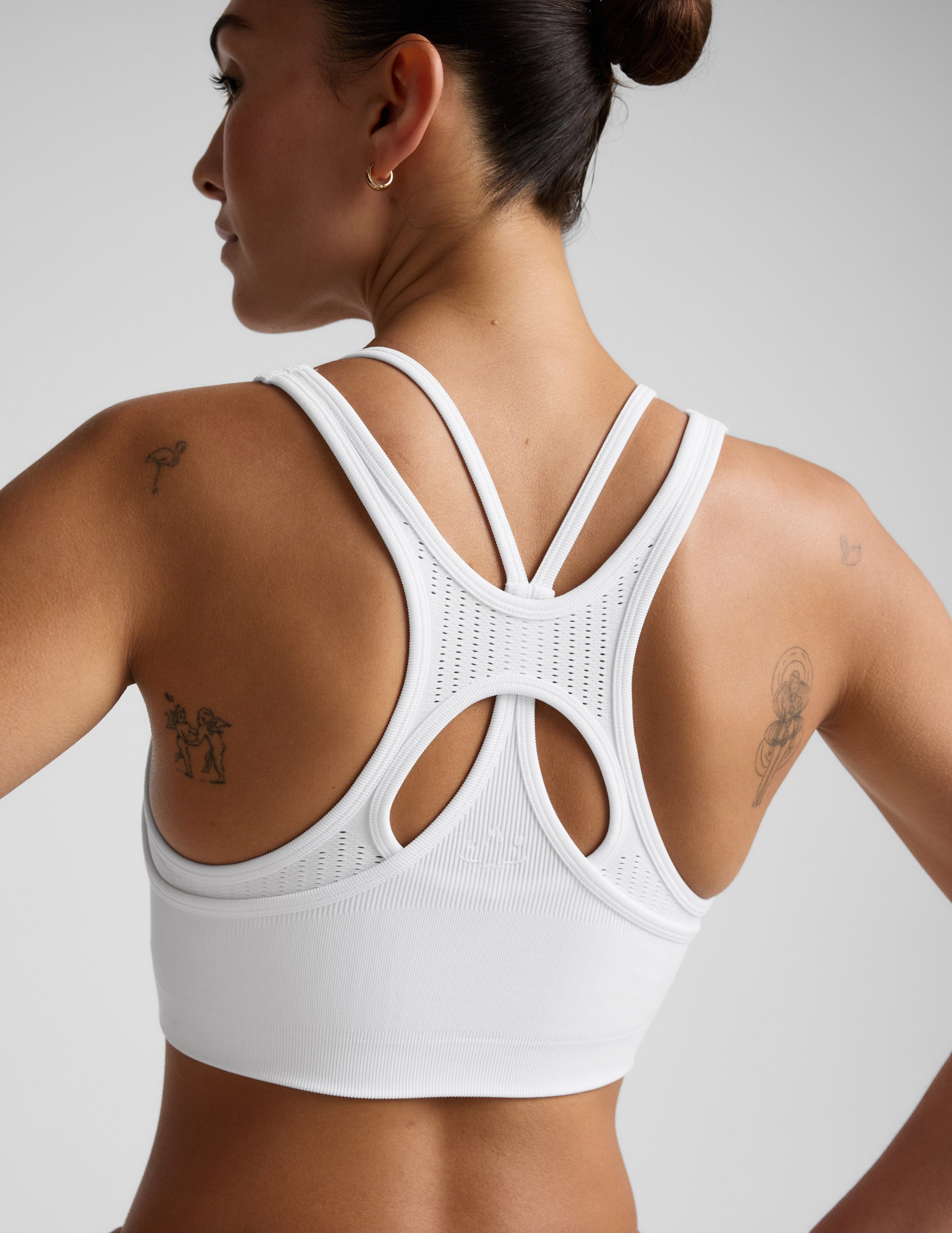 Woman wearing a white sports bra and brown shorts on a plain background.