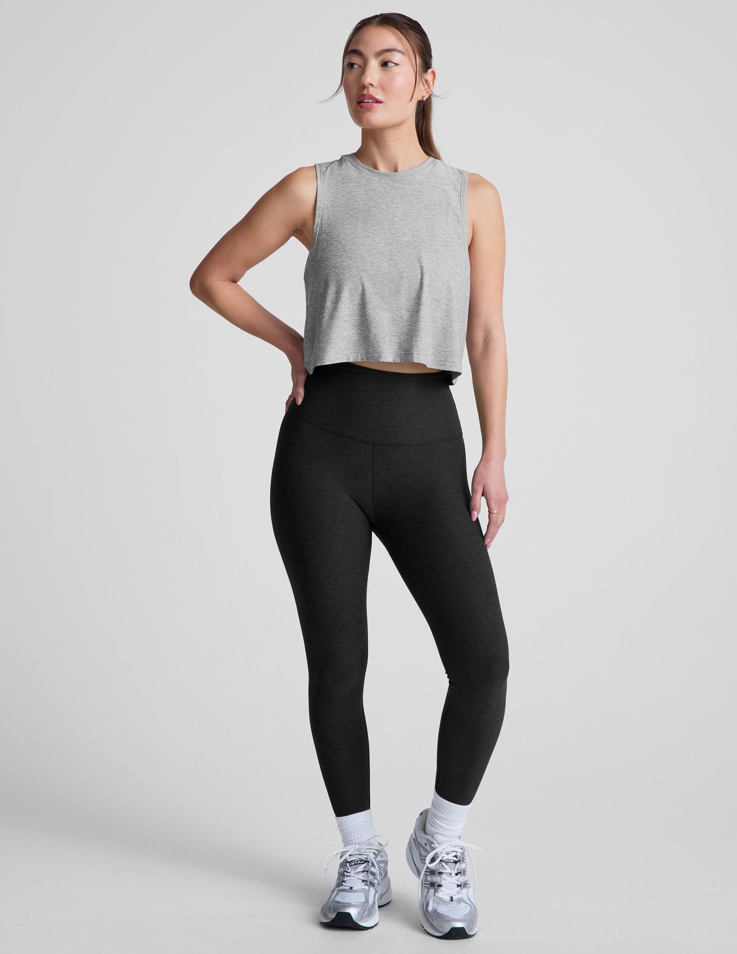 Woman wearing a gray cropped sleeveless top and black leggings on a plain background.