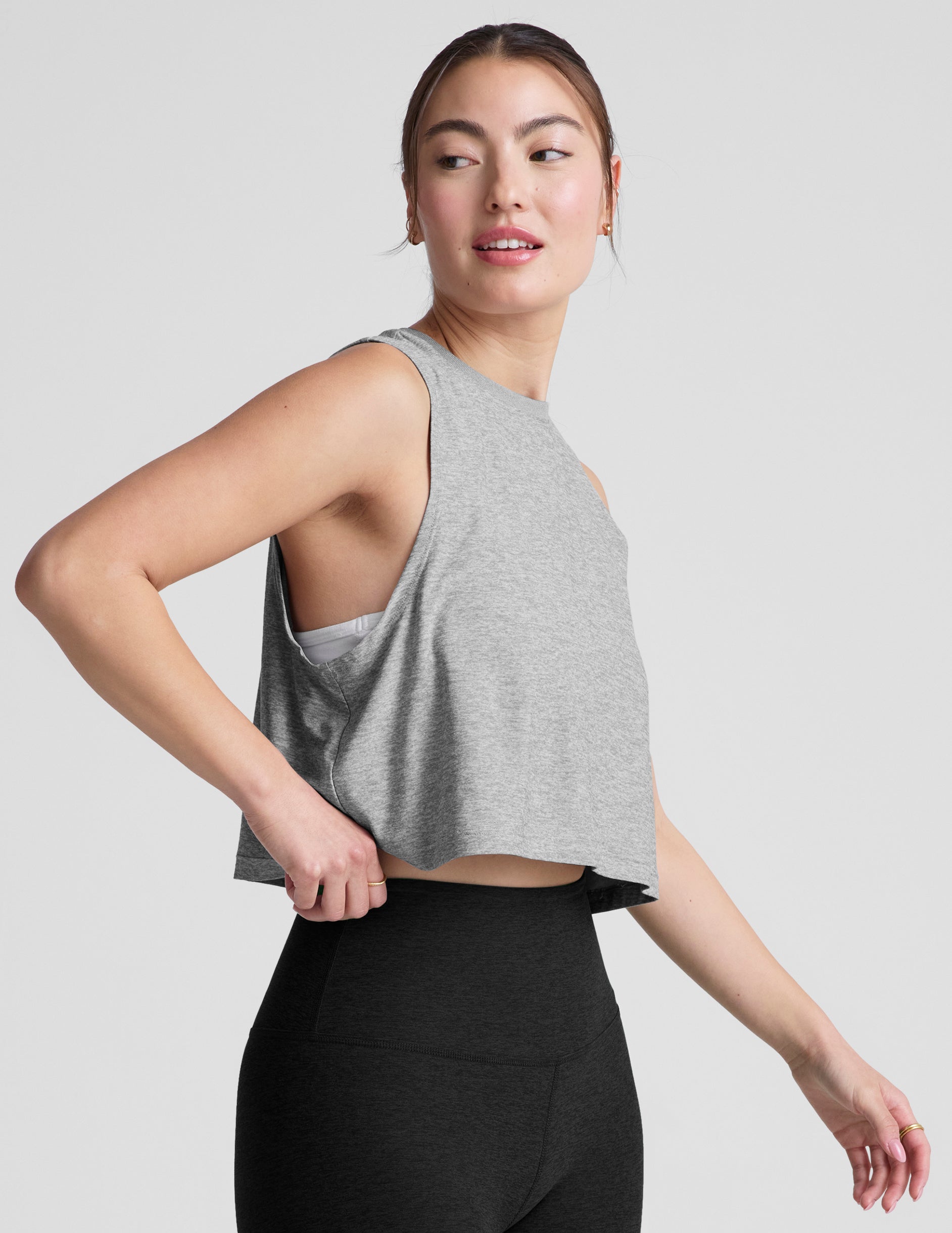 Woman wearing a gray cropped sleeveless top and black leggings on a plain background.