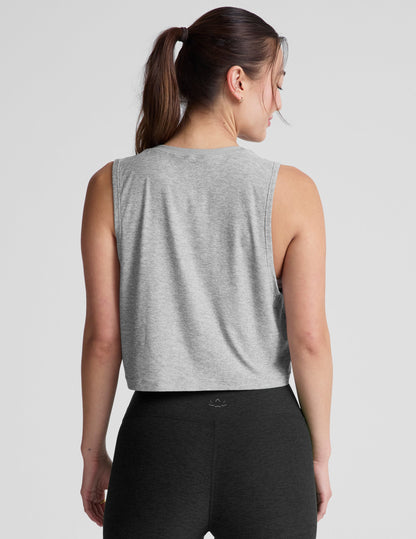 Woman wearing a gray cropped sleeveless top and black leggings on a plain background.