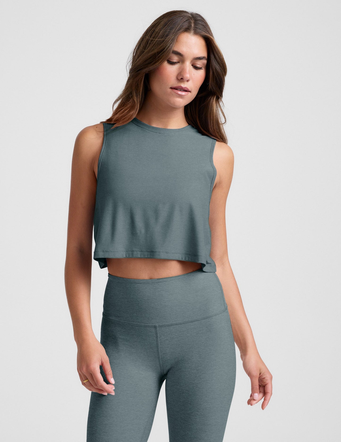 Woman wearing a gray sleeveless top and leggings on a light gray background.