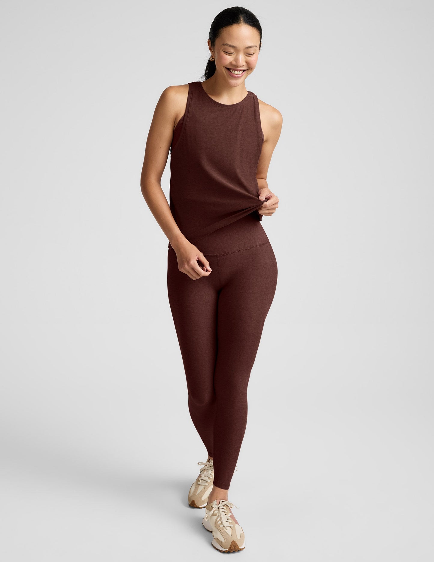 Woman wearing a brown tank top and brown high-waisted leggings against a plain background.