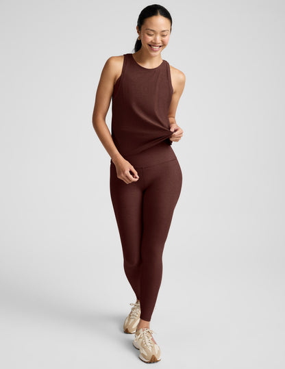 Woman wearing a brown tank top and brown high-waisted leggings against a plain background.
