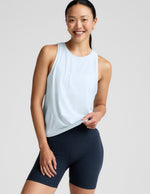 Woman wearing a light blue sleeveless top and navy blue biker shorts on a light gray background.