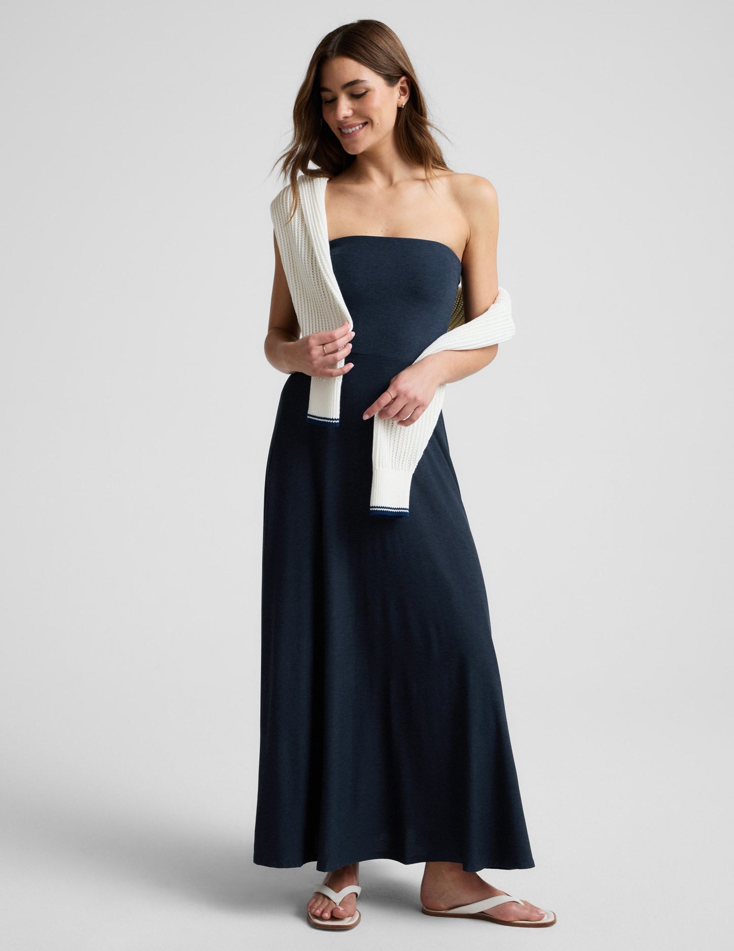 Woman wearing a strapless navy blue maxi dress on a light gray background.
