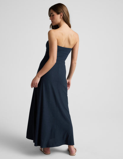 Woman wearing a strapless navy blue maxi dress on a light gray background.