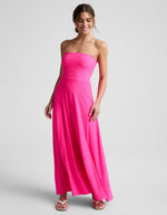 Woman wearing a strapless pink strapless maxi dress on a light gray background.