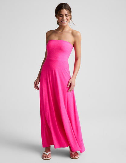 Woman wearing a strapless pink strapless maxi dress on a light gray background.