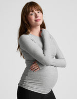 Pregnant woman wearing a gray long-sleeve top against a white background.