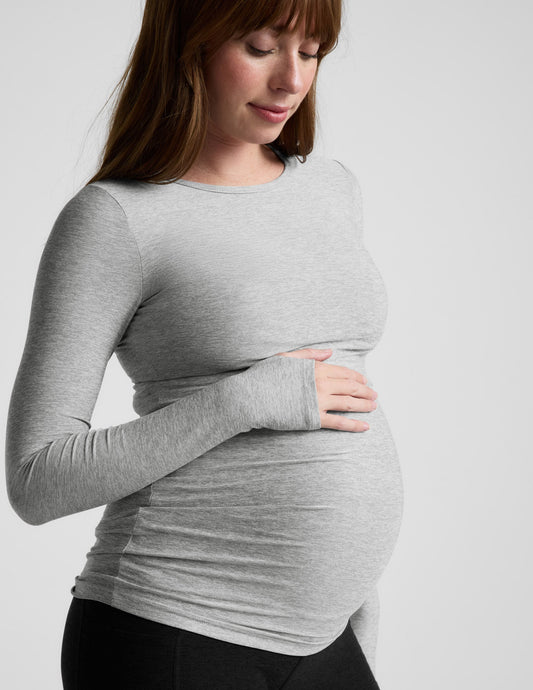 Pregnant woman wearing a gray long-sleeve top against a white background.