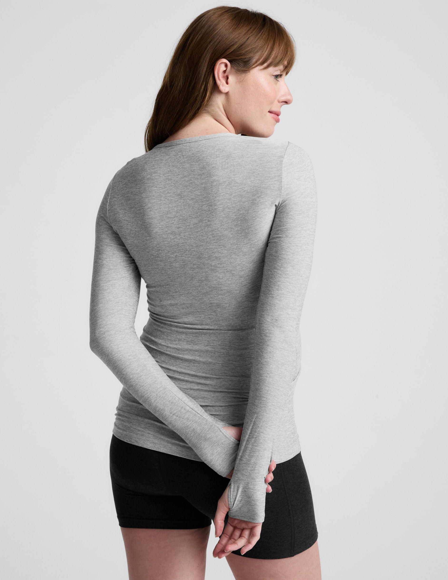 Pregnant woman wearing a gray long-sleeve top against a white background.
