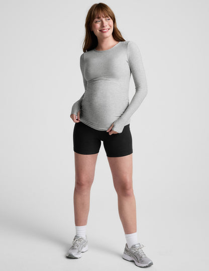 Pregnant woman wearing a gray long-sleeve top against a white background.