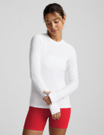 Woman wearing a white long-sleeve top and red shorts on a light gray background.