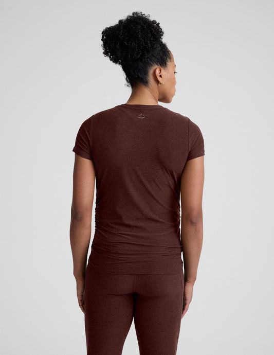 Pregnant woman wearing a brown maternity t-shirt and leggings against a plain background.