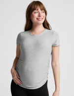 Woman wearing a gray maternity t-shirt and black leggings against a plain background.