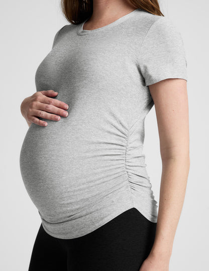 Woman wearing a gray maternity t-shirt and black leggings against a plain background.