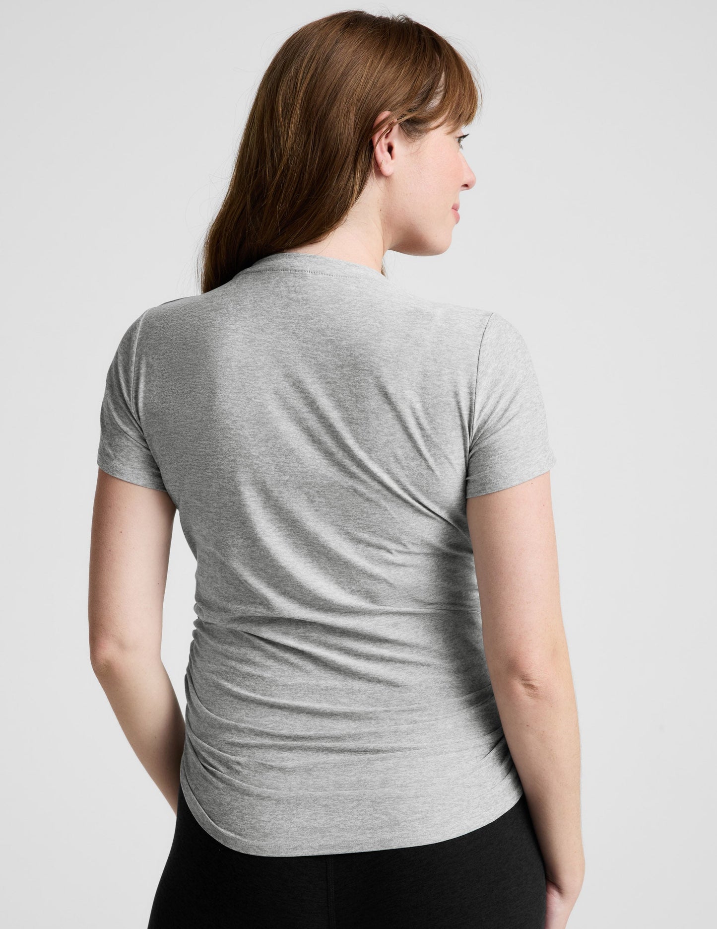Woman wearing a gray maternity t-shirt and black leggings against a plain background.