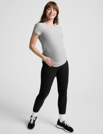 Woman wearing a gray maternity t-shirt and black leggings against a plain background.