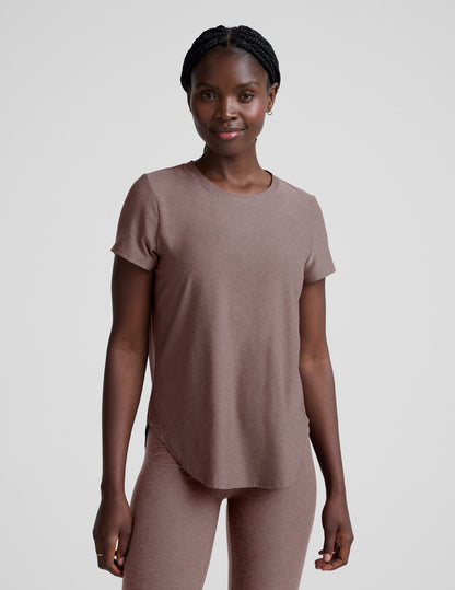 Woman wearing a brown t-shirt and leggings on a plain background.