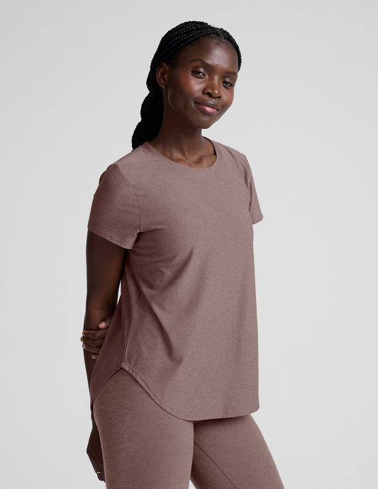 Woman wearing a brown t-shirt and leggings on a plain background.