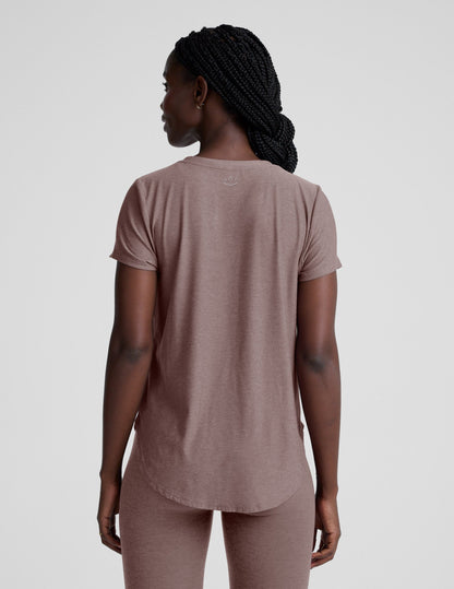 Woman wearing a brown t-shirt and leggings on a plain background.