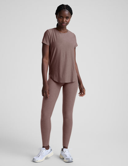 Woman wearing a brown t-shirt and leggings on a plain background.
